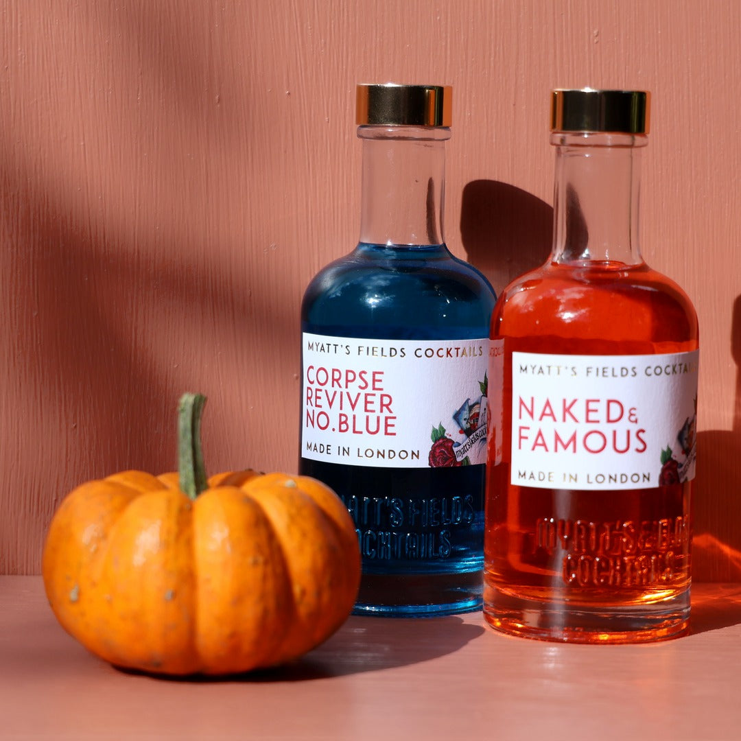 Corpse Reviver No. Blue and Naked & Famous bottles beside a small pumpkin against a terracotta wall